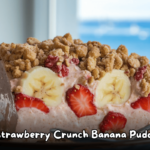 A slice of strawberry crunch banana pudding with layers of fresh strawberries, bananas, creamy pudding, and a crunchy topping, set against a scenic ocean view.